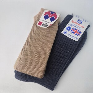 Könnte beinhalten: Zwei Paar Socken werden gezeigt. Ein Paar ist beige mit einem strukturierten Muster, das andere ist marineblau mit einem Rippenmuster. Jedes Paar hat ein Etikett. Das Etikett der beigefarbenen Socken hat ein geometrisches Design, das der marineblauen Socken einen Union Jack.