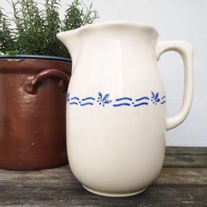Könnte beinhalten: Eine weiße Keramikkanne mit einem blauen und weißen Blumenmuster. Die Kanne hat einen Henkel und einen Ausguss.