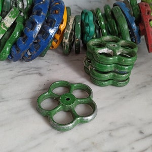 May include: A selection of vintage, flower-shaped valve handles in various colours, including green, blue, and yellow. Some handles are stacked, while others are arranged in a chain. The handles show signs of wear, suggesting they are antique or reclaimed.