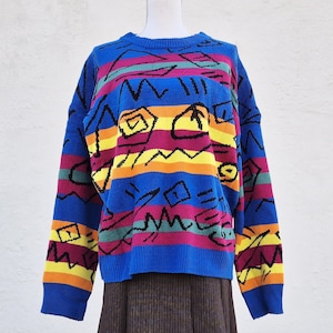 Könnte beinhalten: Ein blauer, mehrfarbiger gestreifter Pullover mit geometrischem Muster. Der Pullover hat lange Ärmel und einen Rundhalsausschnitt.