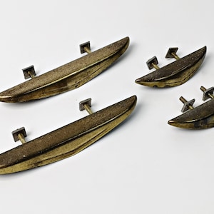 May include: Four brass cabinet pulls with a curved, boat-shaped design. The pulls have a brushed finish and are attached to square metal bases.