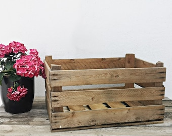 May include: A rustic wooden crate with a natural wood finish. The crate has three horizontal slats and is empty. A bouquet of pink hydrangeas is in a black pot next to the crate.