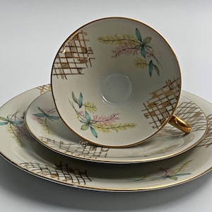 Könnte beinhalten: Ein weißes Tee-Set mit goldener Verzierung und Blumenmuster. Das Set verfügt über ein zartes Blumenmuster mit rosa, gelben und blauen Blüten. Die Untertasse hat ein passendes Muster und einen goldenen Rand.
