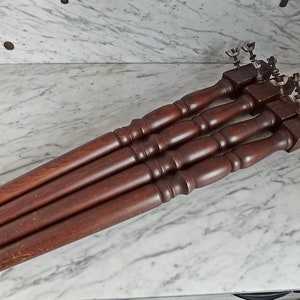 Könnte beinhalten: Vier braune Tischbeine aus Holz mit Metallbeschlägen oben. Die Beine sind in einer Reihe auf einer weißen Marmorfläche angeordnet.