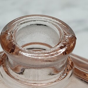 May include: Close-up of the top of a pink glass bottle with a round opening. The bottle has a textured surface.