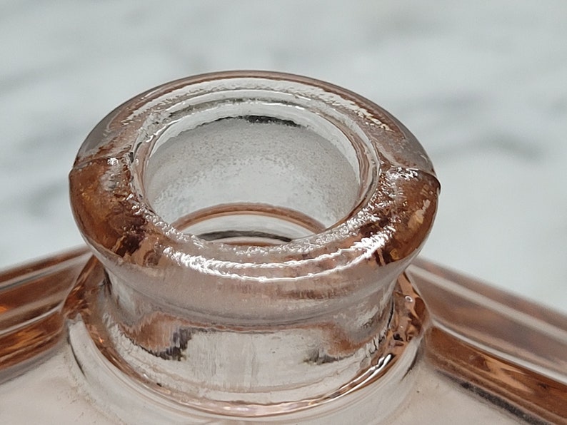 May include: Close-up of the top of a pink glass bottle with a round opening. The bottle has a textured surface.