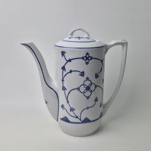 Könnte beinhalten: Weiße Porzellan-Kaffeekanne mit gebogenem Ausguss, Henkel und Deckel. Die Kanne ist mit einem blauen Blumenmuster verziert. Das Design umfasst stilisierte Blumen und Ranken. Die Kaffeekanne ist ein klassisches Design.