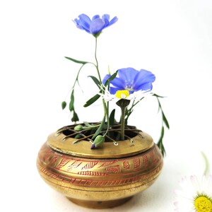 Könnte beinhalten: Ein Messing-Räuchergefäß mit aufwendigen Designs und einer rot-goldenen Oberfläche. Der Brenner ist mit blauen und weißen Blumen gefüllt.