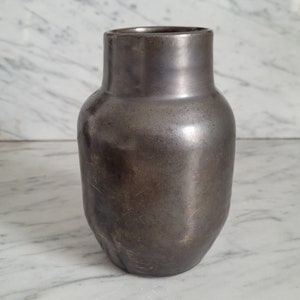 Könnte beinhalten: Eine dunkelgraue Keramikvase mit einer glatten, leicht strukturierten Oberfläche. Die Vase hat eine abgerundete, bauchige Form und eine breite Öffnung.