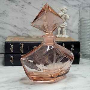May include: A pink glass perfume bottle with a diamond-shaped stopper. The bottle has an etched design and a geometric shape.