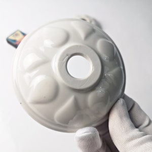May include: White ceramic mould with a scalloped edge and a central hole. The mould has a decorative design of raised, rounded shapes.