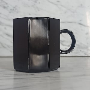 May include: A black hexagonal ceramic mug with a handle. The mug has a glossy finish.