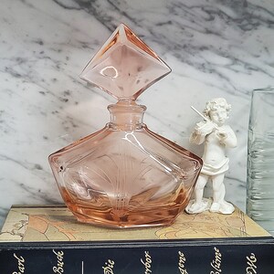 May include: A pink glass perfume bottle with a diamond-shaped stopper. The bottle has a geometric design and is sitting on a book.