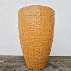 Könnte beinhalten: Eine hohe, orangefarbene Keramikvase mit einer strukturierten, krokodilhautartigen Textur.
