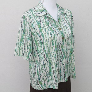 May include: A white short-sleeved shirt with a green, blue, and black abstract pattern. The shirt has a collar and button closure.