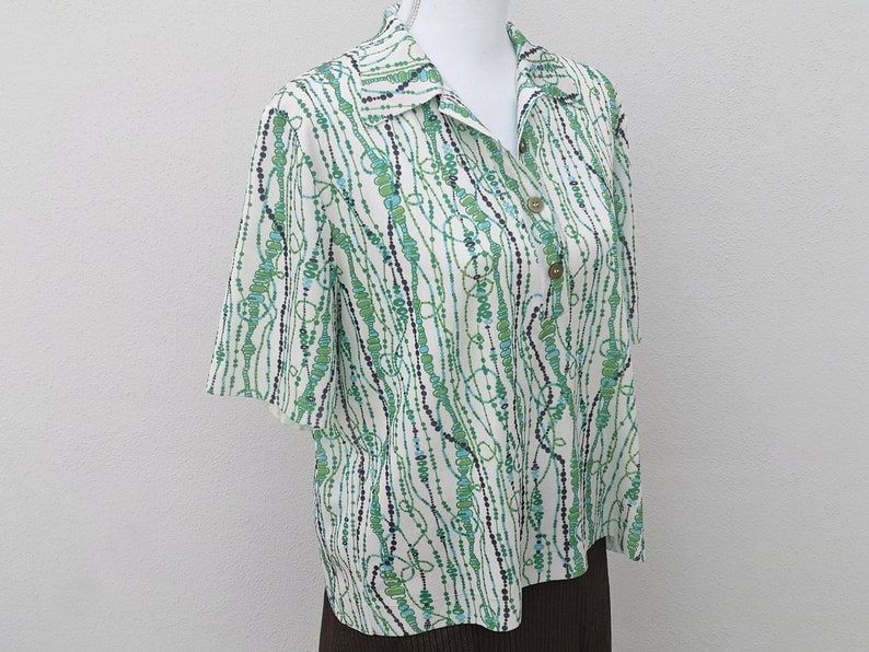 May include: A white short-sleeved shirt with a green, blue, and black abstract pattern. The shirt has a collar and button closure.