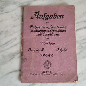 Könnte beinhalten: Ein rosa Buch mit dem Titel "Aufgaben zur Rechtschreibung, Wortkunde, Zeichensetzung, Sprachlehre und Stilbildung" von Richard Lange. Das Buch ist für die 4. Klasse und der 3. Teil der Reihe. Es wurde vom Verlag der Durrschen Buchhandlung in Leipzig herausgegeben.