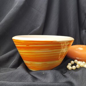 May include: A white ceramic bowl with orange and yellow stripes. The bowl is sitting on a black surface.
