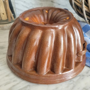 以下が含まれることがあります： フチが波打ったデザインの茶色のセラミック製のバウンドケーキ型。側面に持ち手があり、おいしいバウンドケーキを焼くのに最適です。