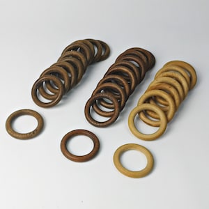 Könnte beinhalten: Holzringe in verschiedenen Braun- und Beigetönen, angeordnet auf einer weißen Oberfläche. Die Ringe variieren in der Farbe, von Dunkelbraun bis Hellbeige. Diese Ringe sind wahrscheinlich für Bastelprojekte oder Dekorationszwecke.
