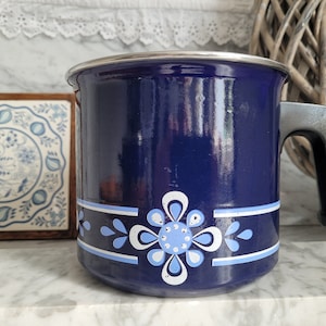 Op de afbeelding: Een blauwe emaille pan met een wit en blauw bloemenmotief. De pan heeft een metalen handvat en een zilveren rand.