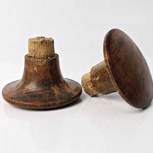 Könnte beinhalten: Zwei Holzgriffe mit einem pilzförmigen Kopf und einer runden Basis. Die Griffe sind braun und haben eine natürliche Holzoptik.