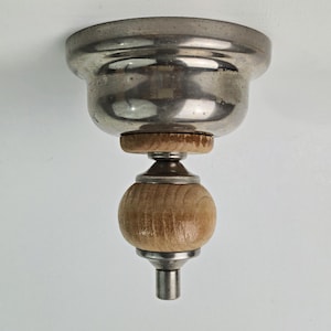 以下が含まれることがあります： 金属製のキャノピーと木製のボール型のアクセントが付いた、ヴィンテージのシーリングライト。 シルバー仕上げで、中央に木の球体があります。 白い天井に取り付けられた照明器具です。