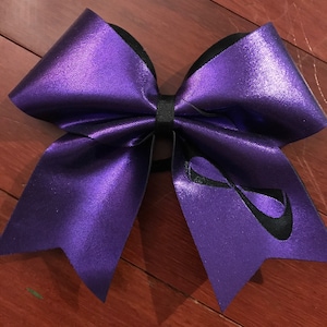 May include: A large purple cheer bow with a black infinity symbol on one side. The bow is made of shiny, metallic fabric.