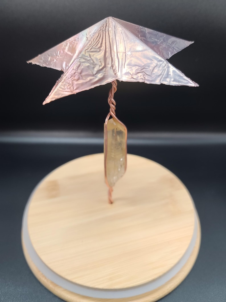 May include: A handcrafted decorative piece featuring a copper wire structure with a star-shaped top and a crystal pendant. The piece is set on a wooden lid, creating a unique and artistic display.