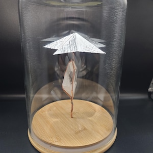 May include: A clear glass cloche with a wooden base houses a quartz crystal suspended by copper wire. A silver foil structure is positioned above the crystal. The cloche sits on a dark surface.