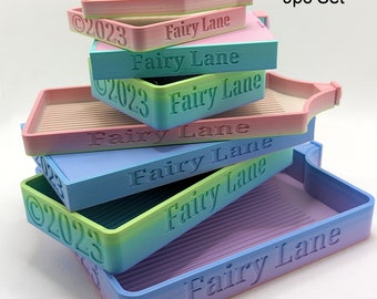 May include: A collection of nine gradient-coloured trays, each bearing the embossed text "Fairy Lane" and "2023". The trays display hues of pink, blue, and green. The set is marked as a "9pc Set".