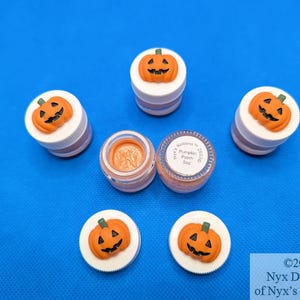 May include: Six small jars with orange pumpkin lids and a white background. The jars contain orange pumpkin paint. The text on the label reads "Nyx's Notions Pumpkin Paint 5oz".