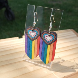 May include: A pair of rainbow striped wooden heart earrings with a silver hook. The hearts have concentric circles of brown, pink, and white.