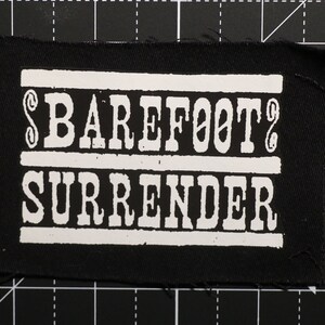 May include: Black fabric patch with white text that reads "$BAREFOOT$ SURRENDER".