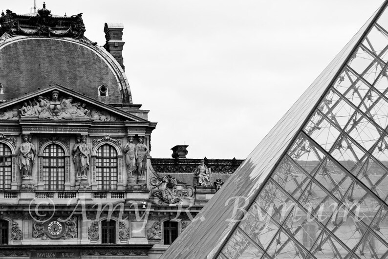 May include: Black and white photo of the Louvre Museum in Paris, France. The iconic glass pyramid is in the foreground, and the classic stone facade of the museum is in the background.