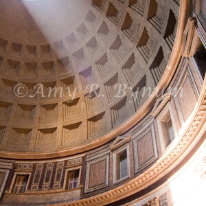 May include: A large, round, domed ceiling with a circular opening at the top. Light shines through the opening, creating a beam of light that illuminates the interior of the dome. The dome is made of stone and has a grid pattern of squares.