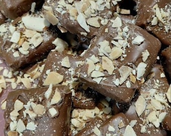 May include: Close-up of chocolate-covered toffee squares, generously sprinkled with chopped nuts. The toffee is a rich brown color, and the nuts are a light tan, creating a visually appealing treat. The image showcases a pile of these delicious confections.