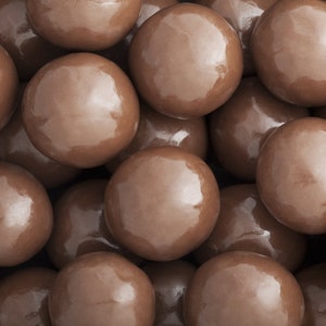 May include: A close-up image of a pile of chocolate candies. The candies are round and brown with a shiny, glossy finish.