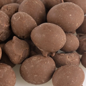 May include: Close-up of a pile of chocolate-covered candies. The candies are a rich, dark brown color and have a smooth, glossy coating. The shapes vary, with some being round and others more irregular.