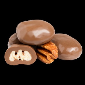 May include: A close-up of milk chocolate pecan candies. The candies are round and have a smooth, glossy finish. One candy is cut in half, revealing the pecan inside.
