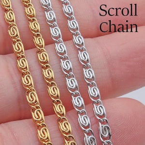 May include: Close-up of gold and silver scroll chains. The chains are made of linked, stylized S-shaped designs. The text "Scroll Chain" is visible in the upper right corner. The chains are displayed against a neutral background.