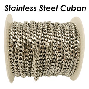 Op de afbeelding: Een spoel met roestvrijstalen Cubaanse ketting. De ketting is zilverkleurig en opgerold rond een witte plastic spoel. De woorden "Stainless Steel Cuban" staan in het zwart bovenaan de afbeelding.