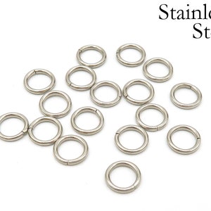 May include: A collection of 15 silver jump rings, made of stainless steel. The rings are all the same size and are arranged in a random pattern on a white background.