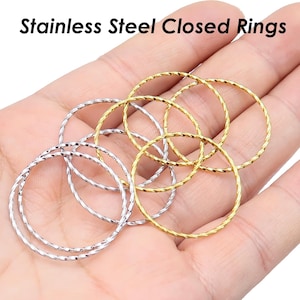 Könnte beinhalten: Ein Satz von sechs geschlossenen Ringen aus Edelstahl, drei goldfarben und drei silberfarben, mit einem gedrehten Drahtdesign. Die Ringe sind in einem Kreis auf einer Hand angeordnet.