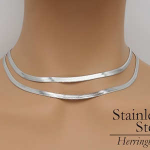 Puede incluir: Un collar de cadena de eslabones de espiga de acero inoxidable plateado. El collar está formado por dos cadenas de diferentes anchos.