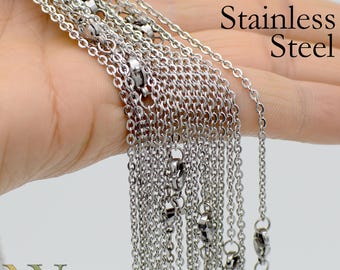 Könnte beinhalten: Nahaufnahme einer Hand, die einen Stapel silberner Edelstahlketten hält. Die Ketten sind alle gleich lang und haben einen Karabinerverschluss. Der Text "Stainless Steel" ist in der oberen rechten Ecke des Bildes sichtbar.