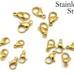 May include: A close-up of 14 gold-toned metal lobster clasps, made of stainless steel. These clasps are commonly used for jewelry making and crafting.