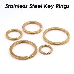 May include: A collection of gold-colored stainless steel key rings in various sizes. The key rings are round and have a split ring design for easy attachment. The text "Stainless Steel Key Rings" is at the top.