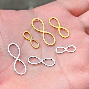 Könnte beinhalten: Eine Sammlung von Unendlichkeitszeichen-Anhängern in Gold- und Silberfarben. Die Anhänger sind in verschiedenen Größen erhältlich und werden auf einer Hand gezeigt. Diese Anhänger eignen sich für die Schmuckherstellung oder Bastelprojekte.