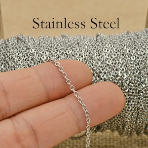 May include: A close-up of a silver chain, made of stainless steel, held in a hand. The chain is coiled up in the background.